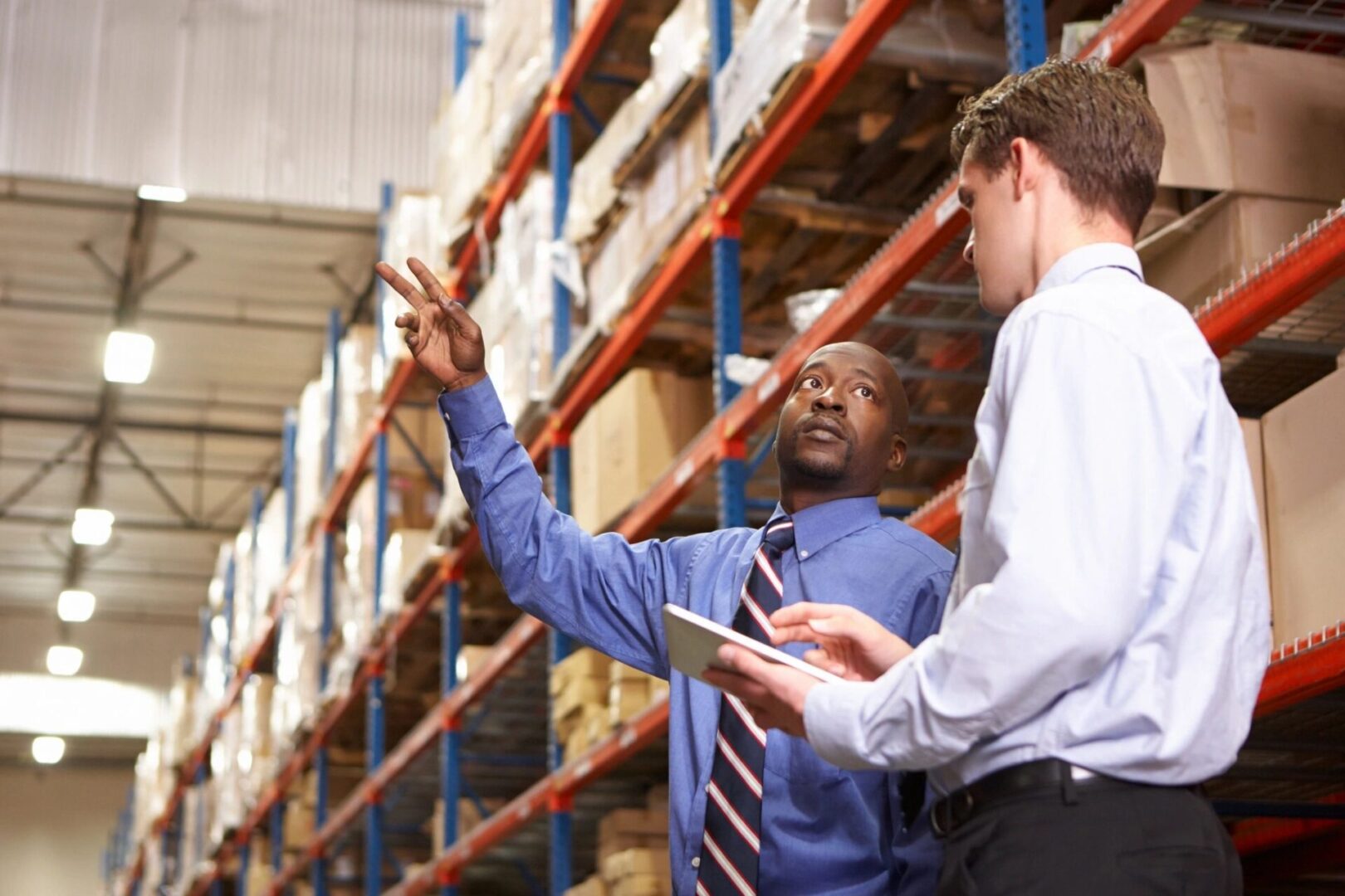 Two men in a warehouse one is holding his hand up to the sky