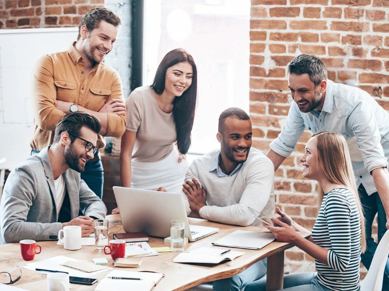 A group of people sitting around a table with a laptop.