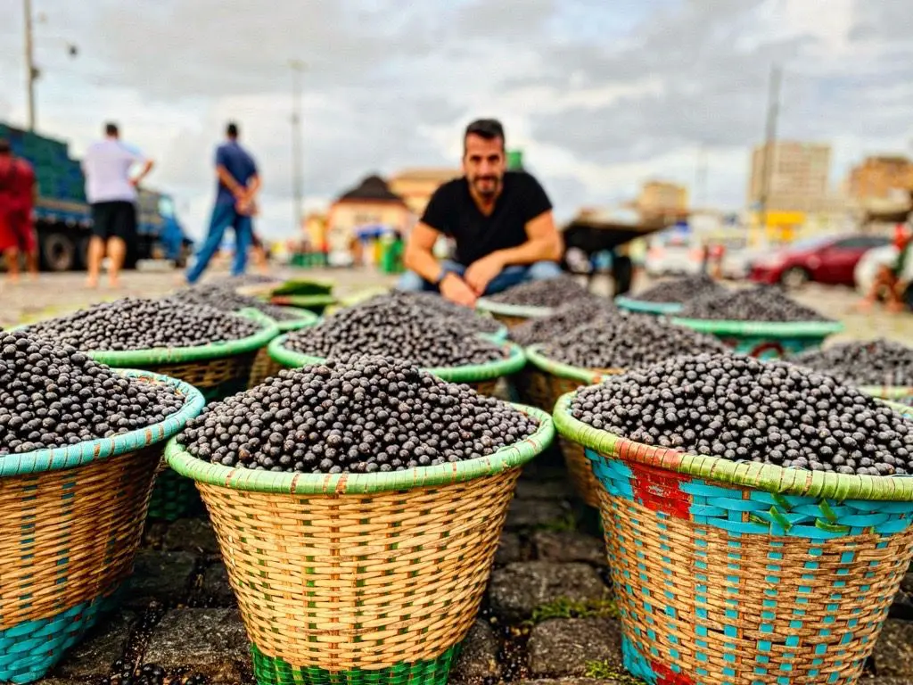 A man sitting in front of baskets filled with black olives.