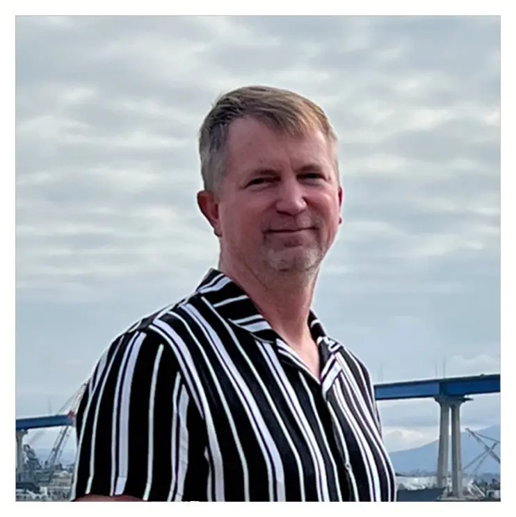 A man in striped shirt standing next to a bridge.